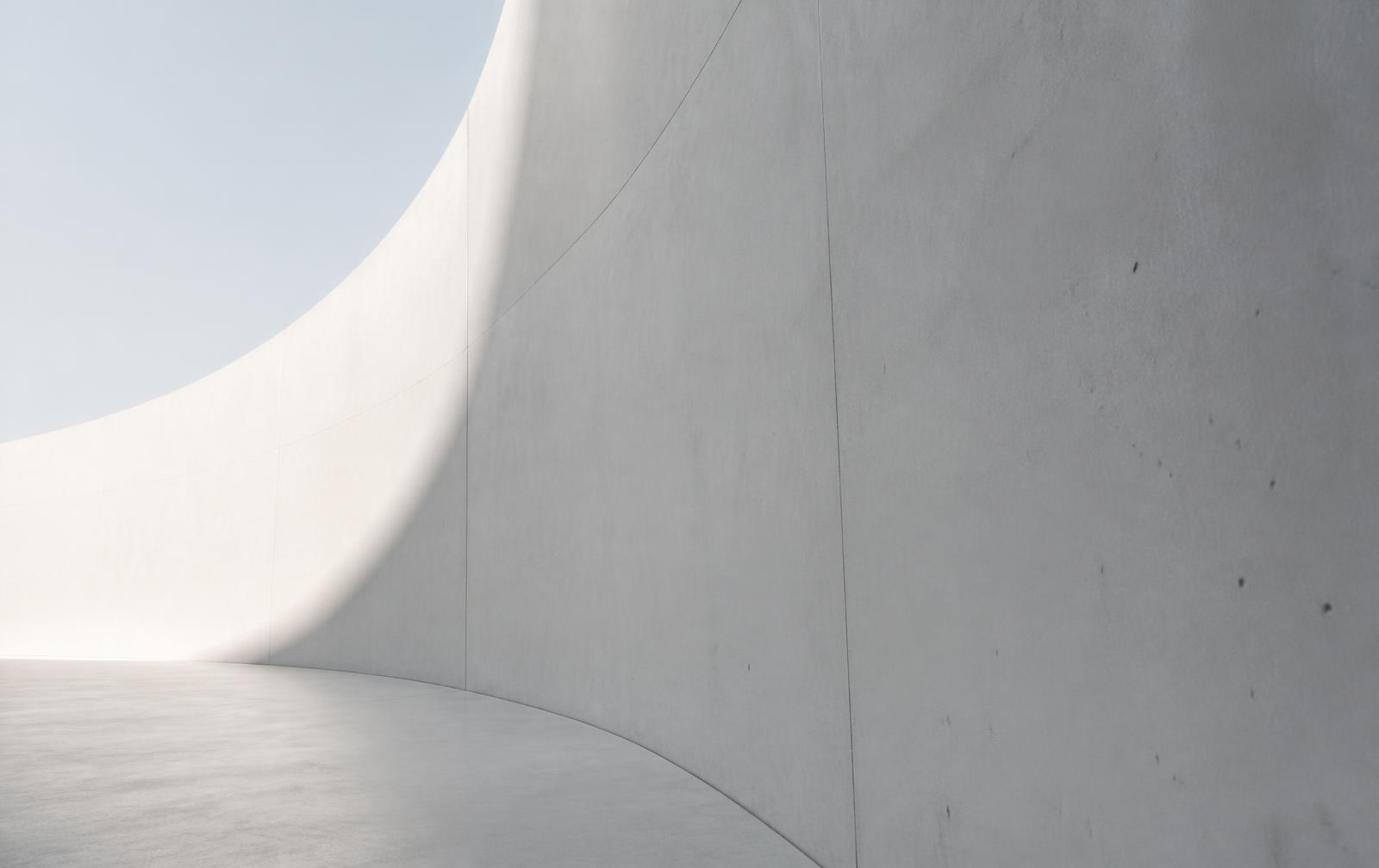A curved white concrete wall meeting the floor in raking daylight